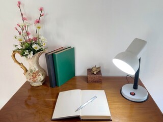 Desk with old book, light bulbs and artificial flower arrangement