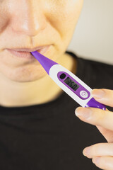 Woman is starting measure temperature at home with electronic thermometer in mouth. Vertical photo.
