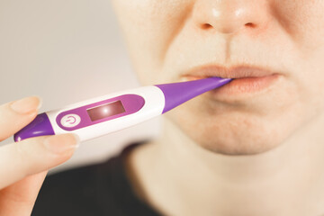 Woman measure temperature at home and hold electronic thermometer in mouth. High body temperature. Colds and flu concept.