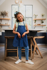 Child girl leaning against kitchen island under pendant lights in farmhouse kitchen wearing apron