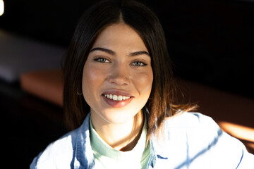 Indian woman sitting on brown bench in cafe wearing denim jacket, mint top under window shadows