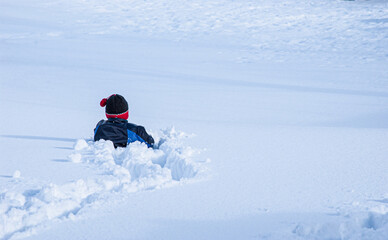 Young child crawling through thick snow in open winter field.