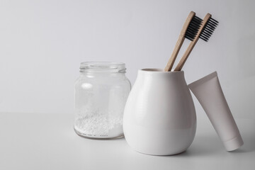 Natural eco friendly toothbrushes in ceramic cup, toothpaste and tooth powder on white background. Dental care, oral health products