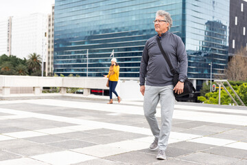 Diverse pedestrians walking across plaza railings holding smartphone and messenger bag, copy space