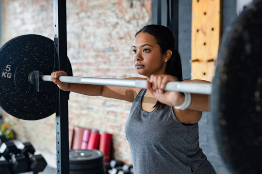 Asian woman wearing sportswear holding loaded barbell with weight plates in gym weight room