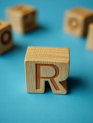 A wooden block with the letter R on it. The block is on a blue surface