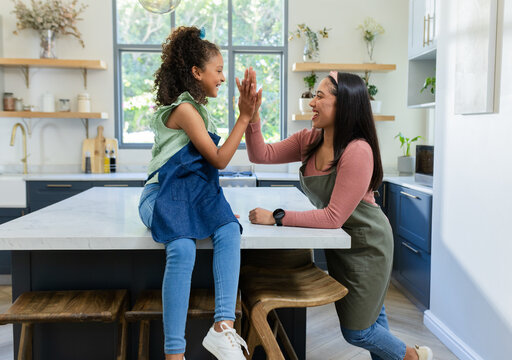Diverse family wearing aprons sharing high-five across marble island in kitchen with gold faucet