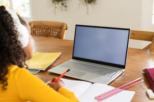 Silver laptop sitting on wooden study table with notebook and red pencil resting by sunlit window