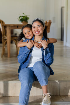Mother and daughter hugging on wooden step in home living dining area wearing denim clothing