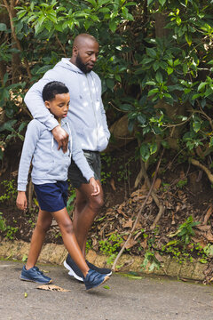 African American father and son walking along paved trail in park wearing hoodies and shorts