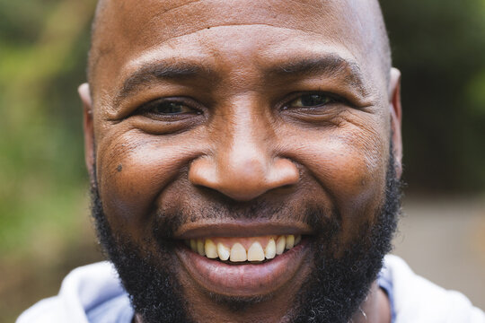 Mature African American male smiling while wearing casual hoodie in park with blurred foliage