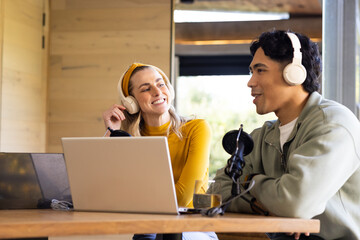 Diverse coworkers recording podcast episode at wooden studio table with laptops and microphone