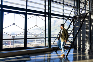 Male standing on ladder in concourse, gazing out through grid windows at mountain view, copy space