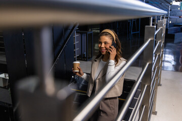 Mid adult professional holding smartphone, sipping coffee on office stairwell, copy space