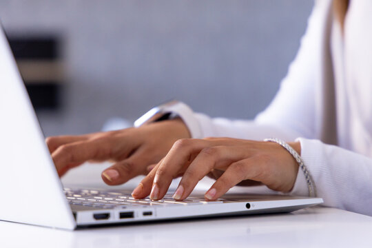 Hands typing on silver laptop keyboard on light desk surface, showing watch and bracelet