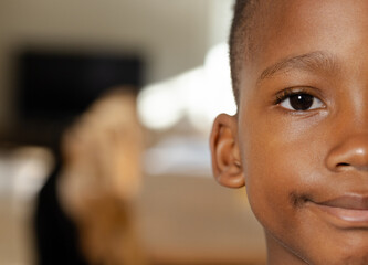 African American child boy smiling gently while sitting on sofa at home with golden dog