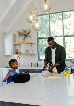 African American father and son preparing sandwich at marble island with board, backpack, notebook