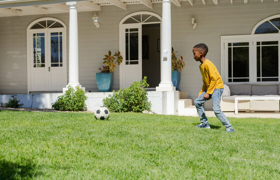 Soccer ball resting on front lawn near porch with blue planters and bright sunlight casting shadows