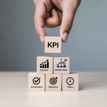 "KPI and Performance Metrics Concept &mdash; Hand Placing 'KPI' Wooden Block on Pyramid of Blocks Featuring Achievable, Measurable, Relevant and Timely Icons &mdash; Business Performance, Goal Setting and Managem