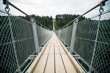 Obraz premium Suspension Bridge Spanning a Valley Canyon on Sunny Day, Adventure and Nature Tourism