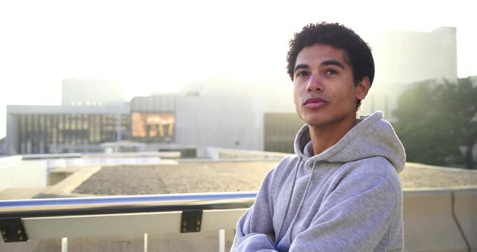 African American Asian man leaning rooftop ledge being backlit by sun smiling, laughing at camera