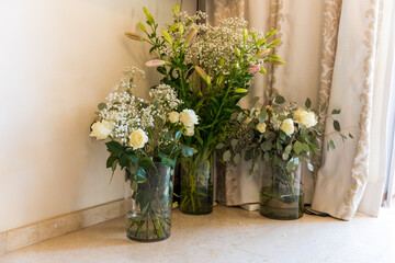 Fresh flowers arranged in vases near a window with curtains during daytime in a bright indoor setting