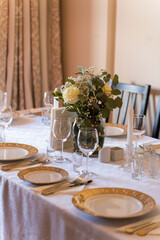 Dining table set for a special meal with floral centerpiece, plates, glasses, and cutlery arranged neatly in a warm indoor setting