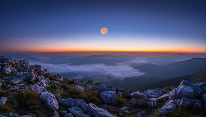 Majestic full moon rising over a tranquil mountain range at twilight, with a breathtaking display of colors across the sky and misty valleys below