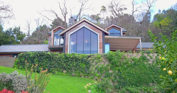 When recording begins, steady camera is panning left across hillside garden to reveal house facade