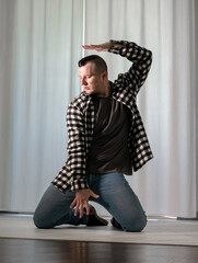 Young guy in a dancing pose on a white background. Modern dance in a plaid shirt. Sports plastic movements of arms and legs and body.