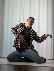 Young guy in a dancing pose on a white background. Modern dance in a plaid shirt. Sports plastic movements of arms and legs and body.