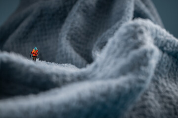 A miniature mountain climber figurine on a fuzzy fleece lining resembling a snow-covered surface, with a blurred background of a mountain or ice wall © Alexander