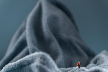 A miniature mountain climber figurine on a fuzzy fleece lining resembling a snow-covered surface, with a blurred background of a mountain or ice wall © Alexander