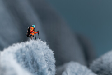 A miniature mountain climber figurine on a fuzzy fleece lining resembling a snow-covered surface, with a blurred background of a mountain or ice wall © Alexander