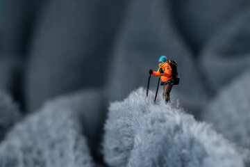 A miniature mountain climber figurine on a fuzzy fleece lining resembling a snow-covered surface, with a blurred background of a mountain or ice wall © Alexander