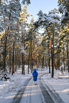 Frau mit Wintermantel beim Spaziergang im verschneiten Wald bei Sonne