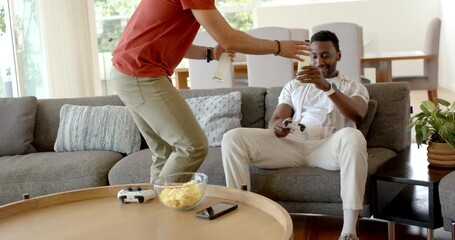 Diverse male friends entering living room, sharing controllers and drinks for staying refreshed