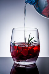 Festive Christmas Snow Globe Cocktail Preparation, Sparkling Water Stream Filling Red Holiday Drink with Cranberries and Rosemary, Winter Beverage Concept for Seasonal Celebration.
