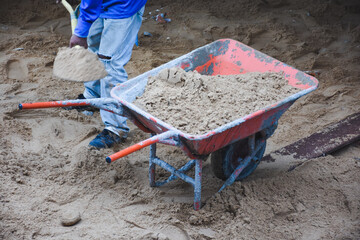 Wheelbarrow next to pile of sand on concrete surface