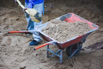Wheelbarrow next to pile of sand on concrete surface