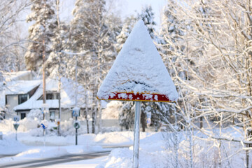 Fototapeta premium Road sign covered in snow. It has snowed so much that the road signs are partially covered. A typical winter landscape in a small Finnish town. Sunny February day.