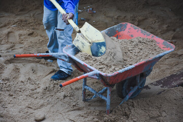 Wheelbarrow next to pile of sand on concrete surface