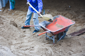 Wheelbarrow next to pile of sand on concrete surface