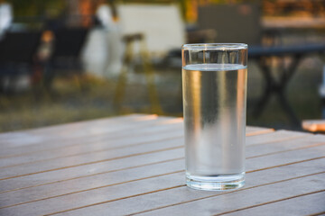 Clear glass of water on a wooden table outdoors.