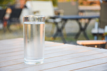 Clear glass of water on a wooden table outdoors.
