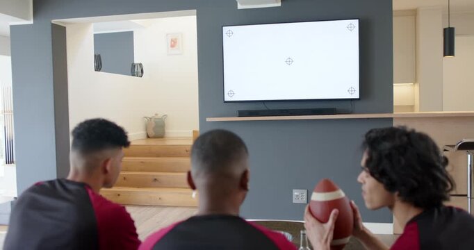 Male friends sitting on sofa watching TV test pattern, jostling football and anticipating broadcast