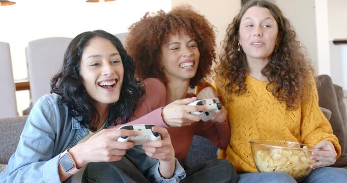 On sofa female friends pressing button starting game grabbing controllers and chips celebrating win