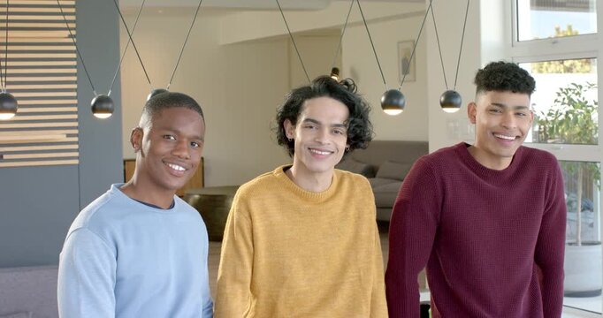 Diverse male friends facing camera leaning, smiling and nodding under pendant lights in living room