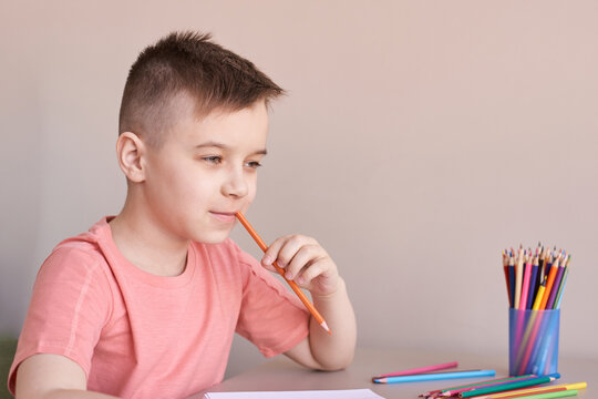 Caucasian young boy thinking while holding pencil in hand at desk with colored pencils.