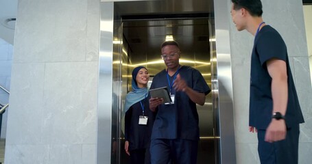 Diverse staff stepping out in lobby as elevator opening with colleague approaching, sharing tablet